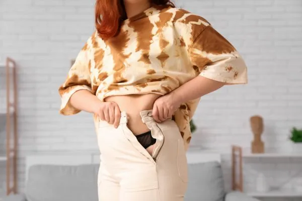 Image of woman trying to do her trousers up after pregnancy weight gain Inverness
