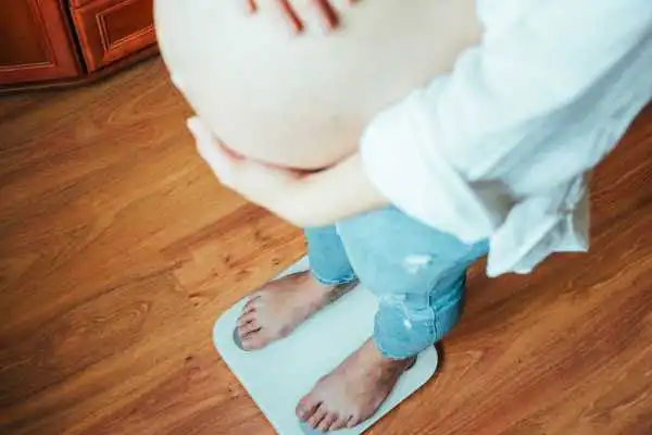 Image of woman weighing herself and experiencing weight gain through pregnancy Inverness